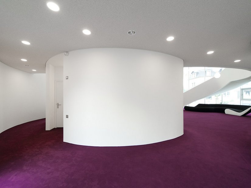 Wie außen dominiert in den Räumen als Wandfarbe Weiß, das edel kontrastiert wird vom kräftigen Aubergineton der Teppichböden.