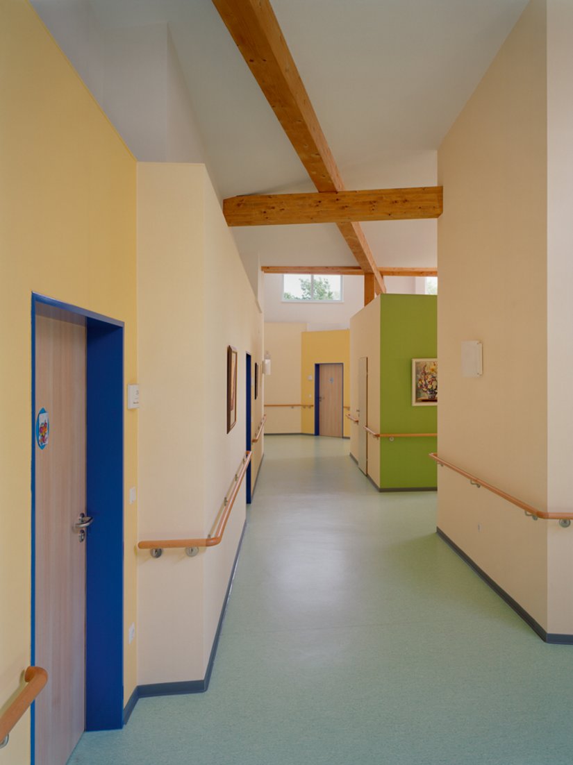<p>Schon von fern markiert ein als Putzmittelraum genutzter Raumwürfel in der Wohngruppen-Leitfarbe den Eingang zum Gemeinschaftszimmer. Der Kubus wird als Galeriefläche genutzt.</p>