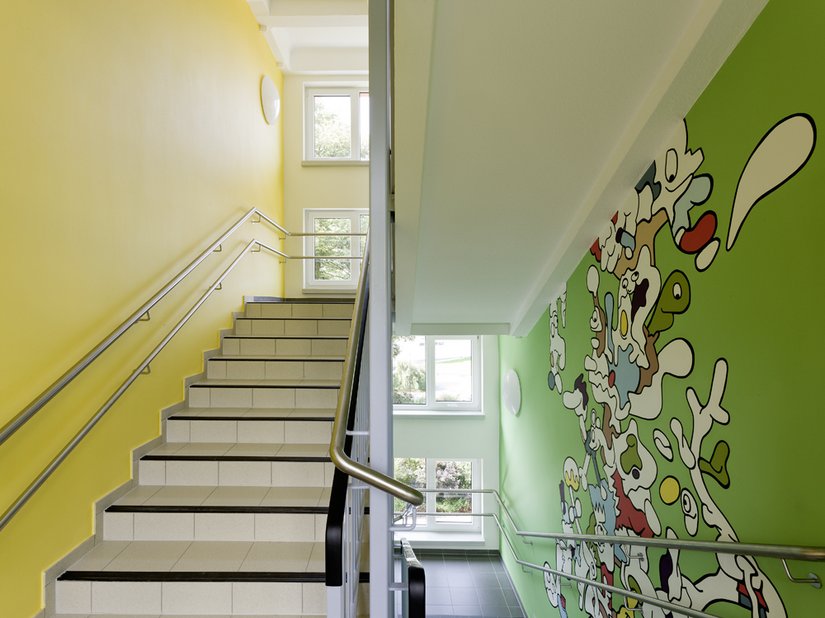 <p>Das Treppenhaus der Grundschule. Der Gestaltungsschwerpunkt liegt hier nicht auf den durchgehenden Stützen, sondern auf der sehr kindgerechten und die Phantasie anregenden Gestaltung von Siebenstein.</p>
