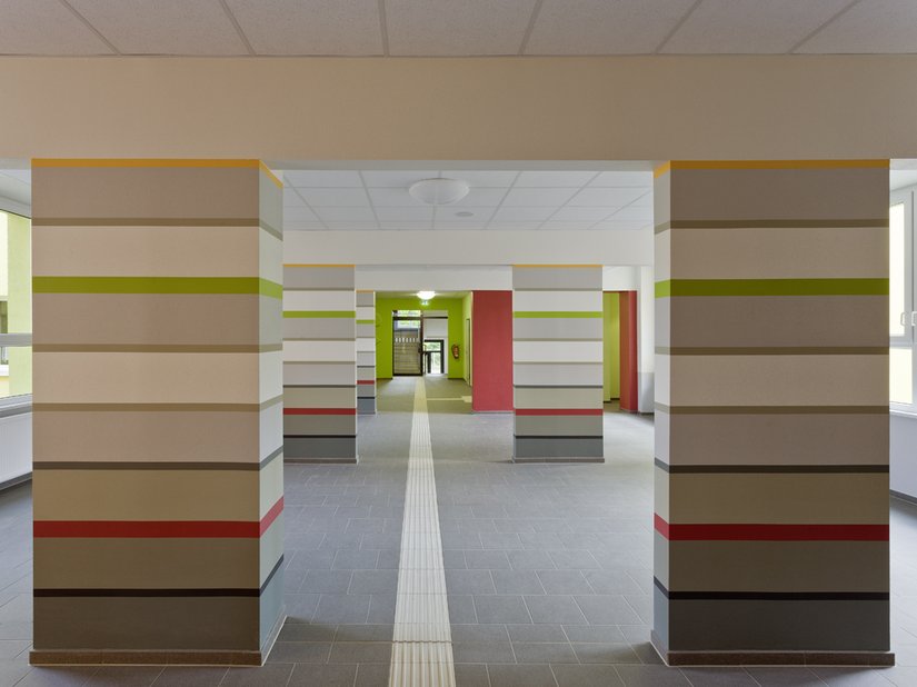 <p>Die einst störenden Wandscheiben wurden das Besondere der Schule. Sie wurden in zur Decke gehörende Unterzüge und Stützen/Pfeiler unterteilt. Letztere wurden durch horizontale Streifen gestaltet, die bewusst durch farbige Bänder getrennt wurden.</p>