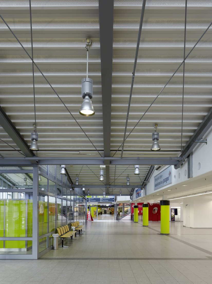 <p>Der helle Deckenanstrich kombiniert mit dem hellen Boden und den leuchten grünen Akzenten auf Augenhöhe lassen die Halle des Paderborn Lippstadt Airports höher wirken.</p>