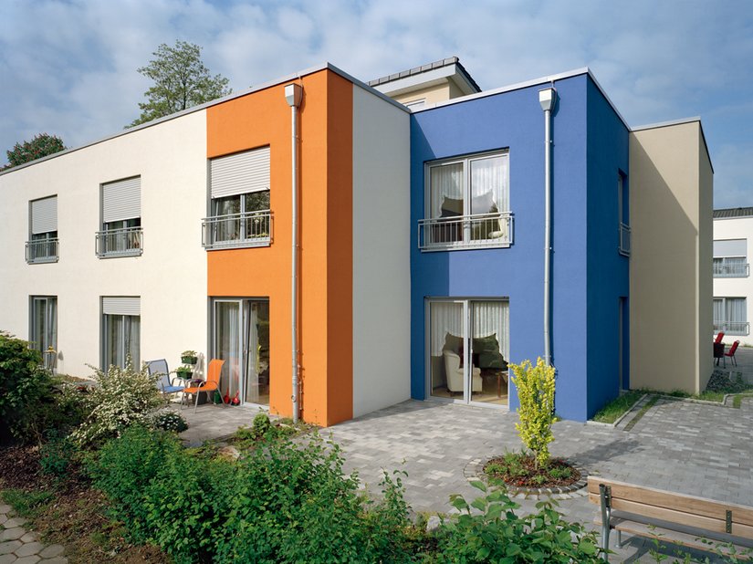 Das satte Orange und das gedämpfte Blau bringen die ansonsten weiß und vanillefarbig gestaltete Gebäudehülle zum Leuchten. Die gestaffelte Architektur, ihre Kuben und die Dimension werden erlebbar.