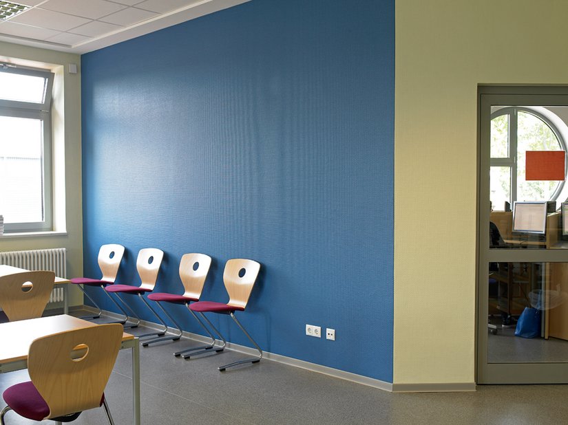 <p>Die blaue Wand ist der „Ruhepol“. Buchefarbene Tische und Stühle werten den Arbeitsplatz auf, und die stoffbezogenen Sitzflächen in angenehmem Rotviolett laden zum Verweilen ein.</p>