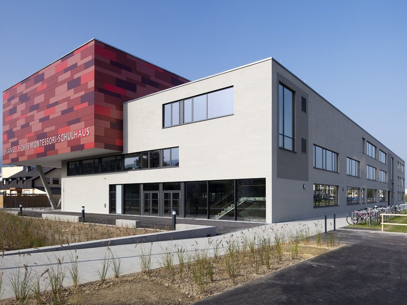 Von weitem wird der Blick auf das Rot der Turnhalle gelenkt, aus der Nähe zieht die Putzfassade des Schulhauses die Blicke auf sich.