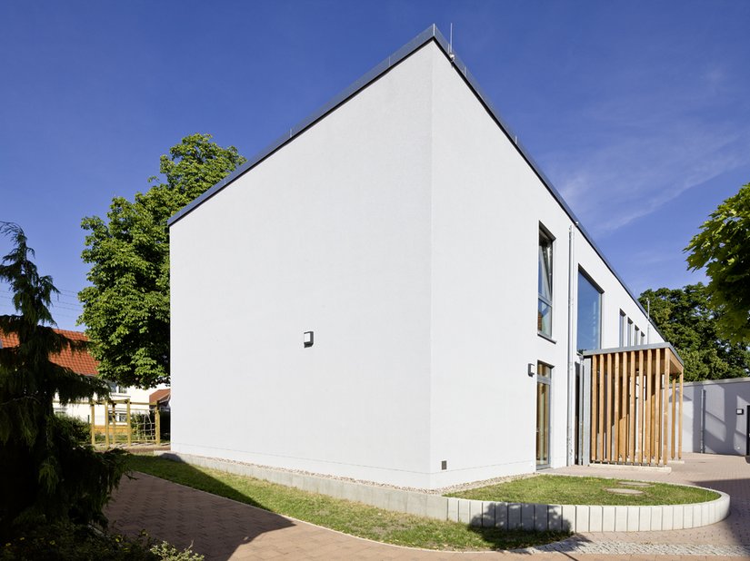 <p>Der hölzerne Eingangsbereich nimmt die Farbigkeit des nebenstehenden Gebäudes auf.</p>