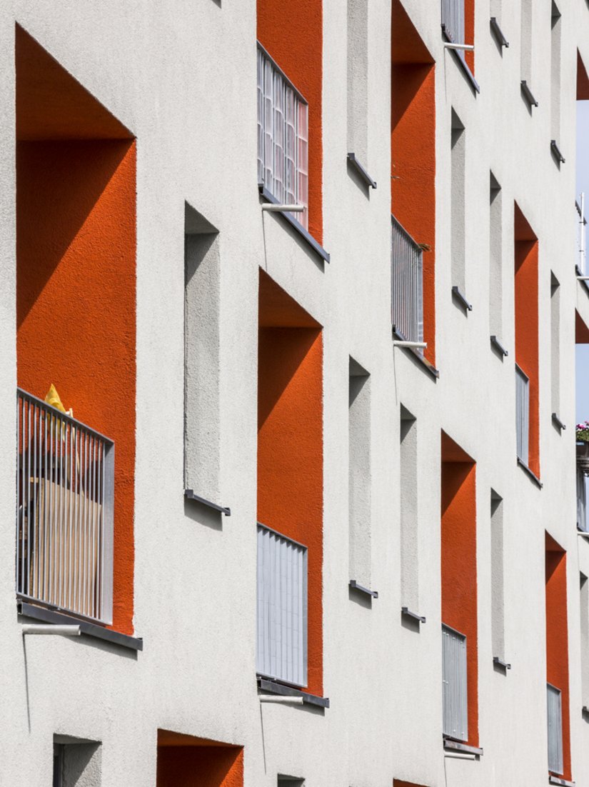 <p>Die hellgraue Fassade wird durch markante orangerote Loggien unterbrochen.</p>