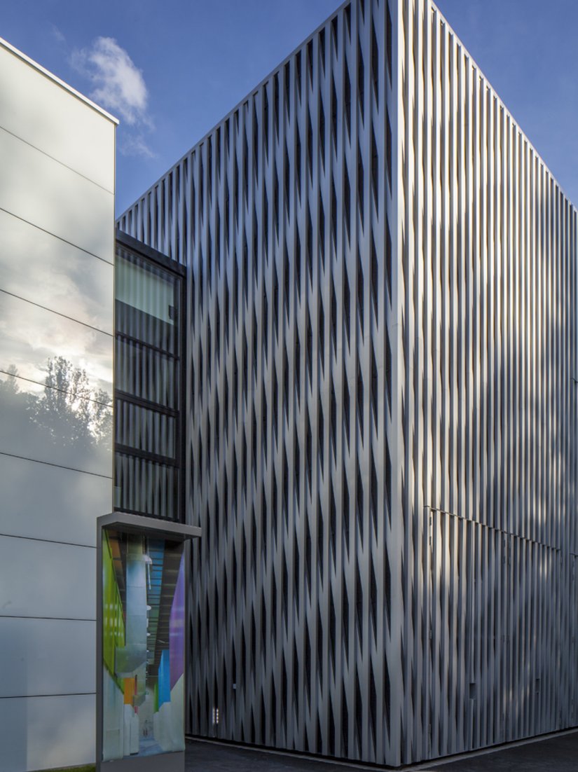<p>Der L-förmige Bürobau mit horizontalen Fensterbändern umschließt die Aluminiumfassade der Halle.</p>