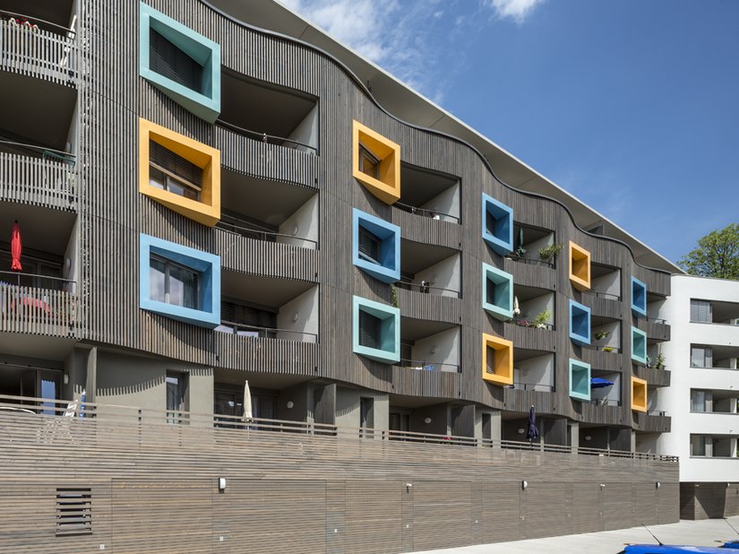 <p>Die Fassade wird hier zu einer gewellten Haut aus Holz, in der Balkone und farbige Guckkästen der einzelnen Wohnungen integriert sind.</p>