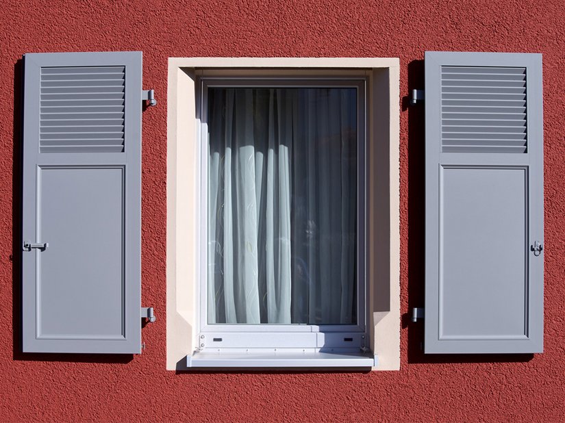 Weitere Betonung der Fenster: Die in&nbsp; Grau aufbereiteten Läden ziehen den Blick auf die Fassadenöffnungen und geben dem Haus sein unverwechselbares Erscheinungsbild. Die in Crème beschichteten Faschen rahmen die Fenster zusätzlich ein. Um sie von den roten Kratzputzflächen abzusetzen, wurde der Glattputz Mineral-Leichtputz G 3679 verarbeitet.