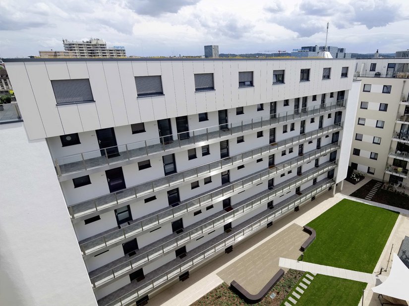 Das Staffelgeschoss mit den Maisonette-Wohnungen wird durch die hochmoderne Metallfassade in Weißmetallic betont.