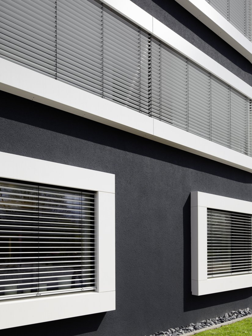 <p>Die plastisch betonte, weiße Umrahmung der horizontalen Fensterbänder integriert den außenliegenden Sonnenschutz und den notwendigen, horizontalen Fensterschluss in die Fassadenkonstruktion.</p>